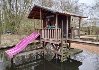 Houten huisje met roze glijbaan en speeltoestel