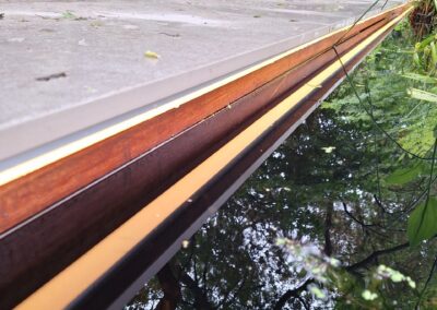 Een close-up van een smal waterkanaal omzoomd door steen en hout, dat het omringende groene gebladerte weerspiegelt. De scène creëert een illusie van verticale diepte met weelderig groen op de achtergrond. Gemaakt door de werkverzetter